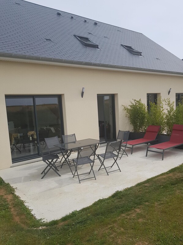 Un bâtiment moderne doté d’un toit plat, de grandes portes-fenêtres coulissantes et d’un patio aménagé avec du mobilier d’extérieur.