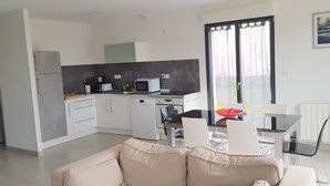 A modern kitchen with white cabinets, a microwave, and a dishwasher. There is a dining area with a glass table and chairs.