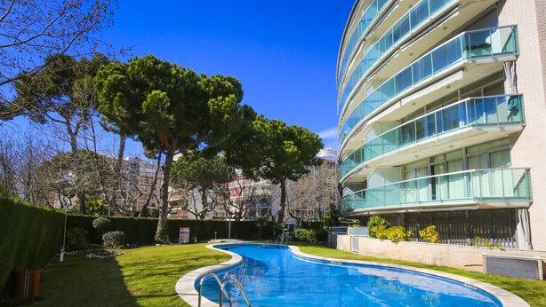 A modern building with a swimming pool surrounded by well-maintained grass and trees. - Apartment in the city centre, with pool and A/C (Salou)