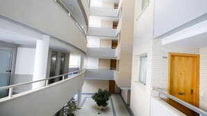 A multi-level interior corridor with a central potted plant, white walls, and a wooden door. - Apartment in the city centre, with pool and A/C (Salou)