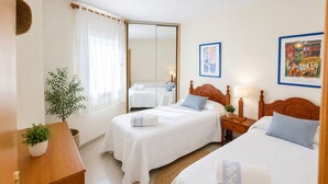 A hotel room with two beds, a wooden headboard, a bedside table with a lamp, a potted plant, and a large mirror. - Apartment in the city centre, with pool and A/C (Salou)