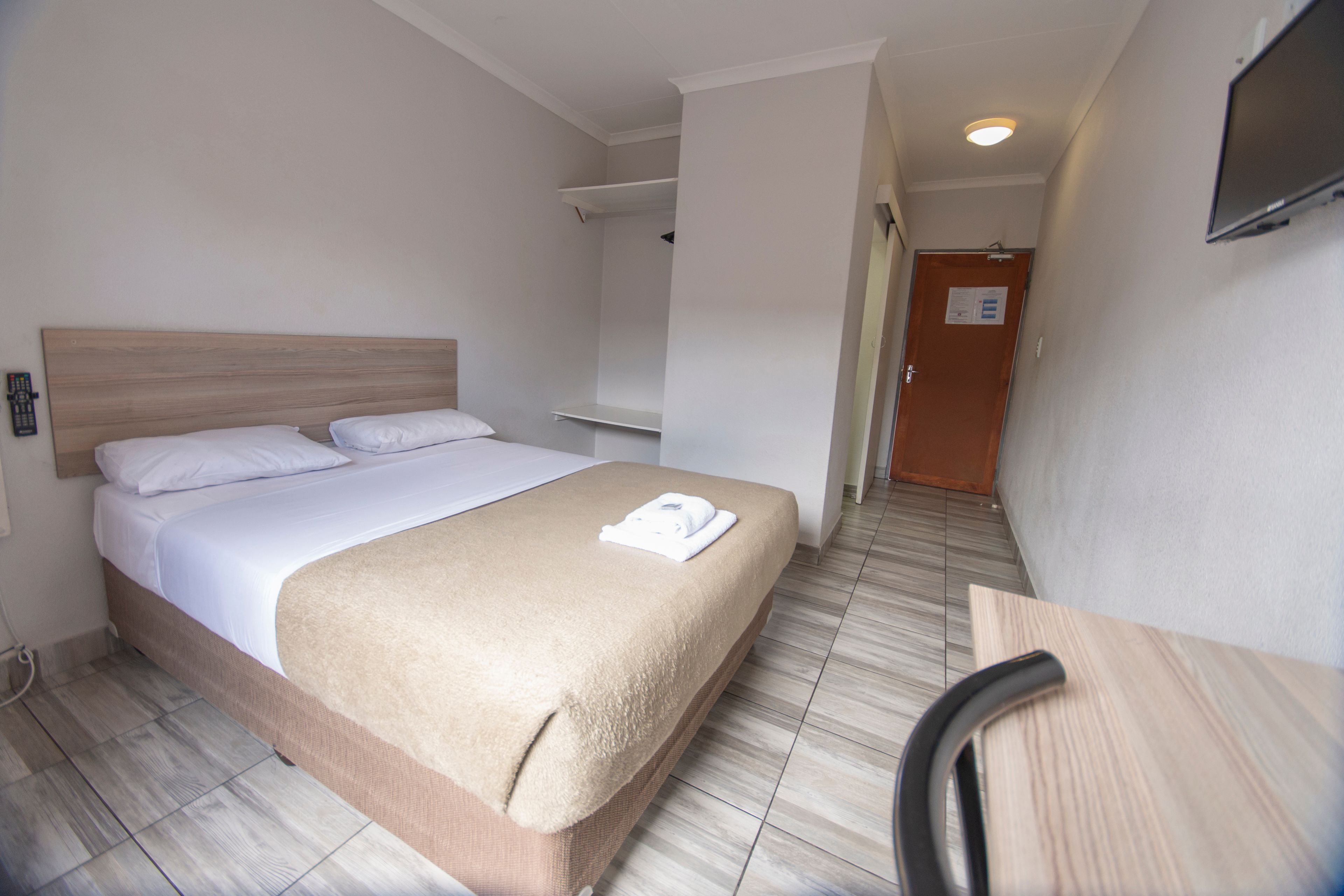 A hotel room with a bed, a desk, a chair, and a television on the wall.