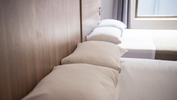 Una habitación de hotel con cabecera de madera, cama con sábanas blancas y ventana con cortinas.