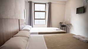 Habitación de hotel con dos camas, un escritorio, una silla, un televisor y una ventana con cortinas.