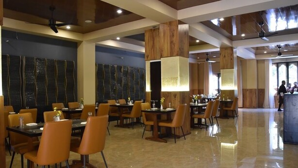 Uma ampla sala de jantar com várias mesas e cadeiras, detalhes em madeira e piso polido.