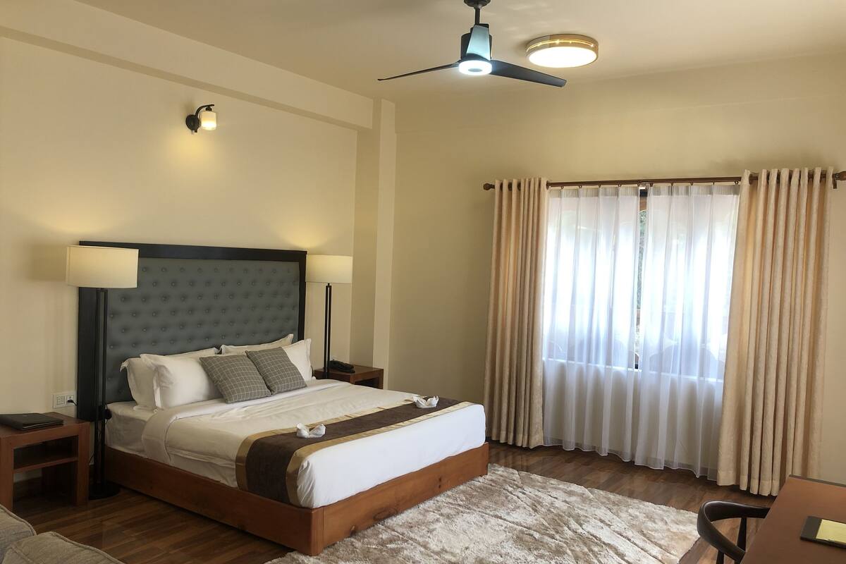 A hotel room with a large bed, two bedside lamps, a ceiling fan, and a window with curtains.