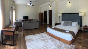 Quarto de hotel com cama, sofá, escrivaninha, televisão e ventoinha no teto.