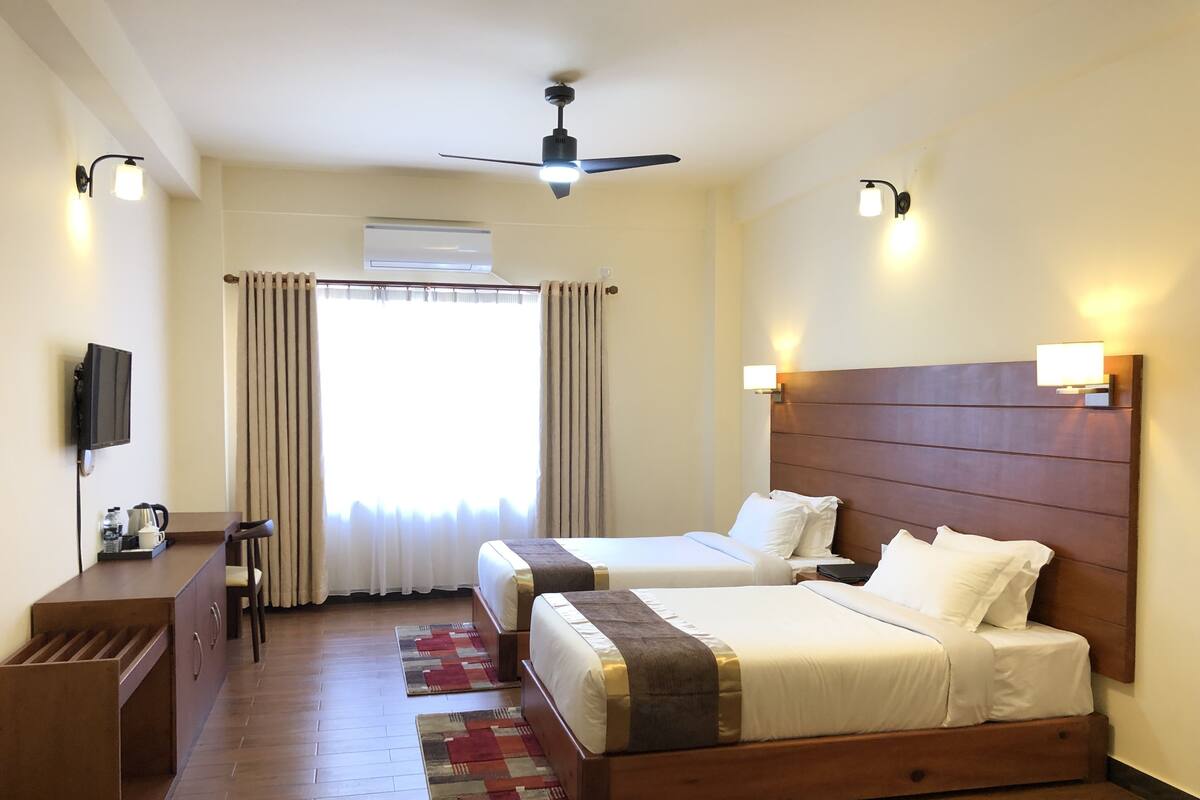A hotel room with two beds, a desk with a chair, a television, and a ceiling fan.
