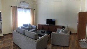 Uma sala de estar moderna com um sofá cinzento, uma mesa de centro e uma TV sobre um móvel de madeira.