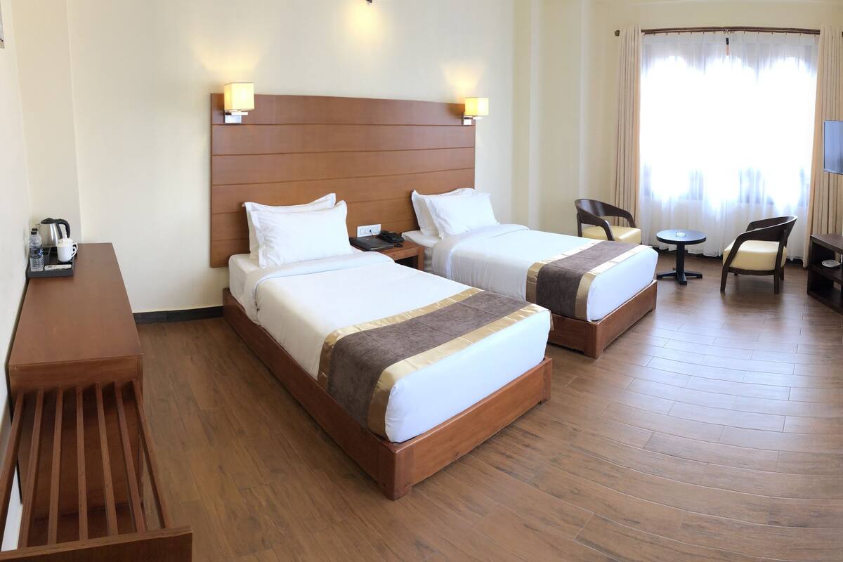 A hotel room with two beds, a desk, a chair, a TV, and a window with curtains.