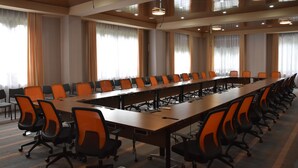 Uma sala de conferências com uma mesa longa, várias cadeiras e grandes janelas com cortinas.