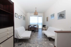 A room with a bed, a desk, a chair, a table, and a view of the sea.