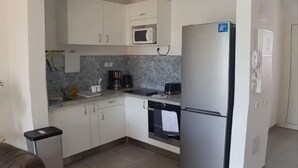 Eine kompakte Küche mit weißen Schränken, einer Mikrowelle, einem Kühlschrank, einer Kaffeemaschine und einem Spülbecken.