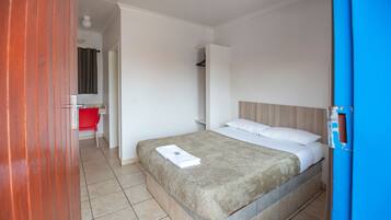 A hotel room with a bed, a red chair, a small table, and a bathroom visible through an open door.
