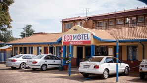 A motel with a reception area, several parked cars, and a brick building with a tiled roof. - Ecomotel Germiston (Germiston)