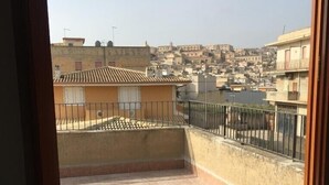 A rooftop terrace with tiled flooring and a metal railing, overlooking a densely packed urban area with traditional buildings. - Simonetta's Rooms (Noto)