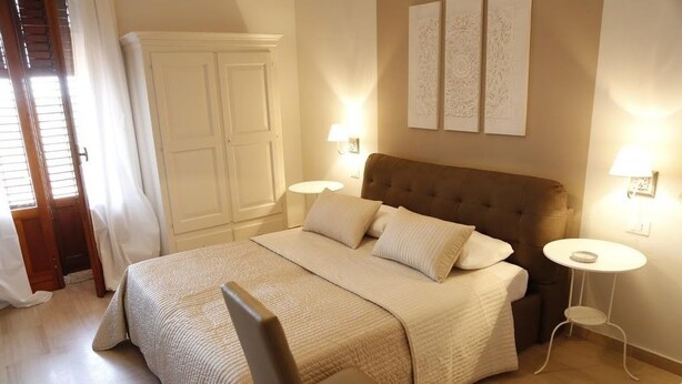 A bedroom with a large bed, two bedside tables, a wardrobe, and artwork on the wall. - Simonetta's Rooms (Noto)