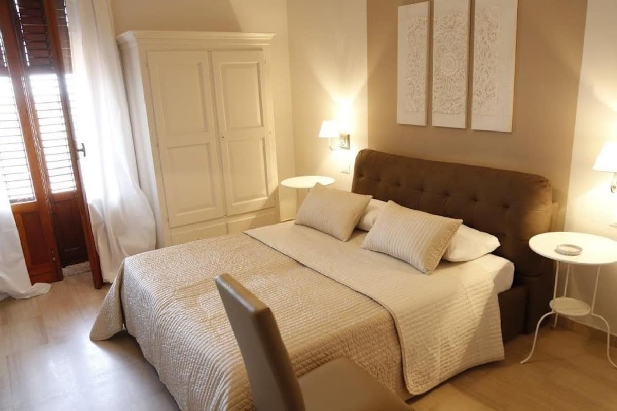 A bedroom with a large bed, two bedside tables, a wardrobe, and artwork on the wall.