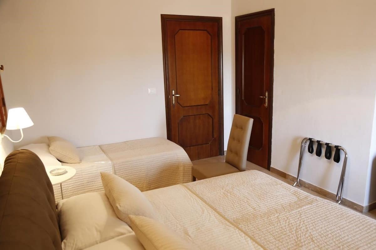 A hotel room with two beds, a chair, a desk, and a coat rack.