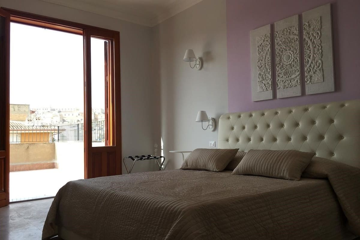 A bedroom with a large bed, a balcony, and decorative wall art.
