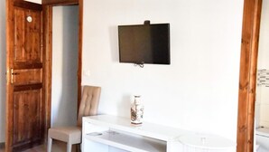 A room with a wooden door, a white chair, a white console table with a vase, and a flat-screen TV mounted on the wall. - Simonetta's Rooms (Noto)