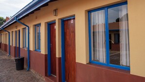 A row of hotel rooms with wooden doors and blue trim, a trash bin, and a brick-paved walkway. - Ecomotel O.R Tambo Intl (Kempton Park)