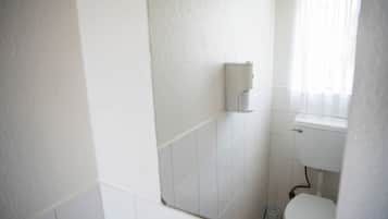 A small, clean bathroom with white tiles, a toilet, and a hand dryer mounted on the wall.