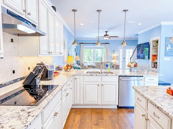 A modern kitchen with white cabinets, granite countertops, a built-in oven, and a dishwasher.