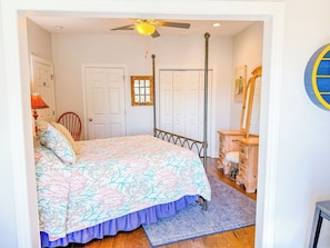 Un dormitorio con cama, ventilador de techo, cómoda y puerta.