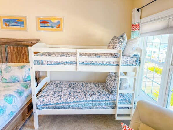 A bunk bed room with floral bedding, a wooden headboard, and two beach-themed wall art pieces.