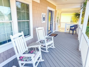 A porch with two rocking chairs and a table, a door, and a window.