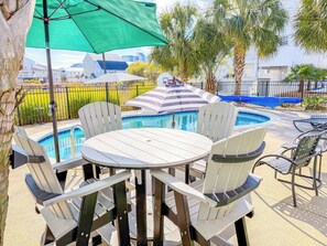 A poolside area with a round table and chairs, a pool, and a green umbrella.