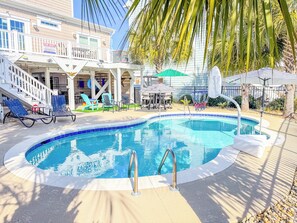 A swimming pool with a sun deck, lounge chairs, and a covered seating area.