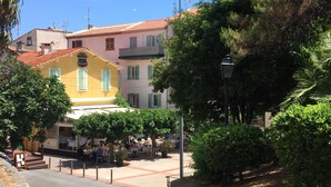 A yellow building with a red-tiled roof, surrounded by greenery and a paved area with tables and chairs. - CHARMING T2 IN THE HEART OF THE OLD TOWN - QUIET - 100 M SEA AND MARKET (Antibes)