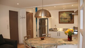 A dining area with a round table, chairs, a vase with flowers, a hanging light fixture, a refrigerator, a sink, and a door. - CHARMING T2 IN THE HEART OF THE OLD TOWN - QUIET - 100 M SEA AND MARKET (Antibes)