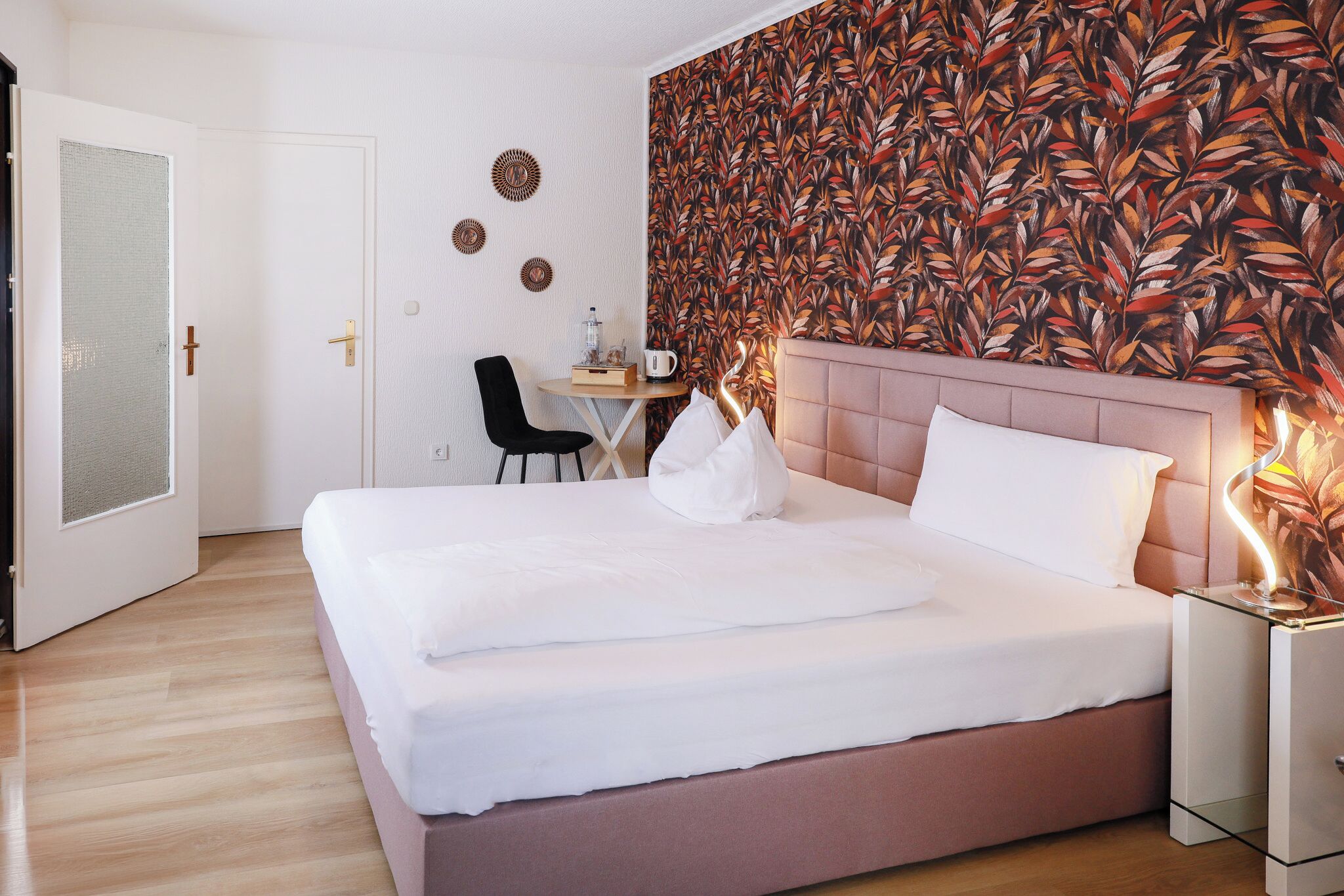 A hotel room with a bed, a desk, a chair, and a wall with a leaf pattern.