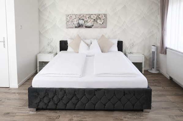 Una cama bien hecha con un cabecero oscuro, ropa de cama blanca y dos mesitas de noche con lámparas.