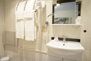 Une salle de bain avec un lavabo blanc, un miroir et un porte-serviettes sur lequel sont disposées plusieurs serviettes.