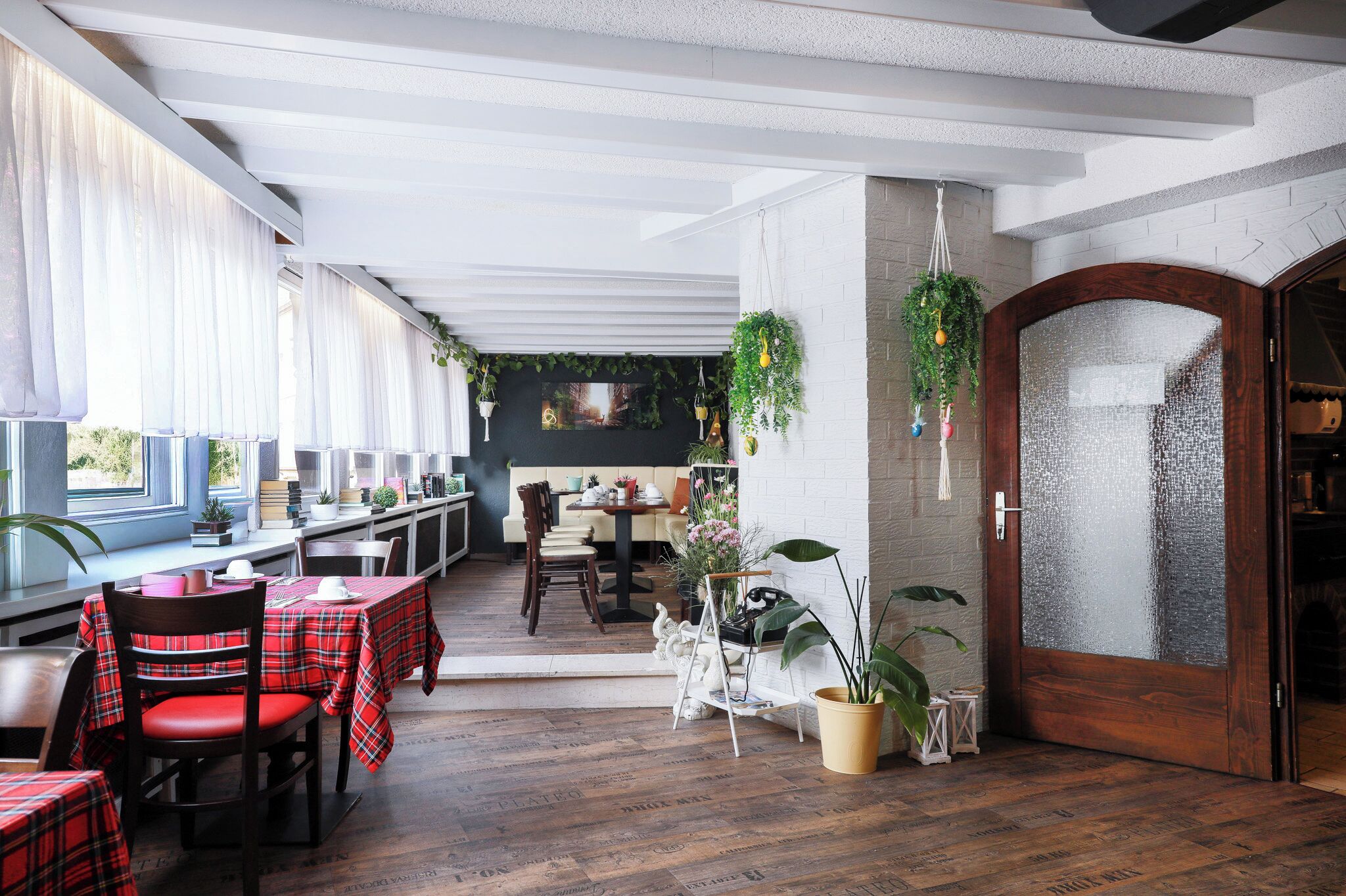 A restaurant with a long counter, red plaid tablecloths, and wooden flooring.