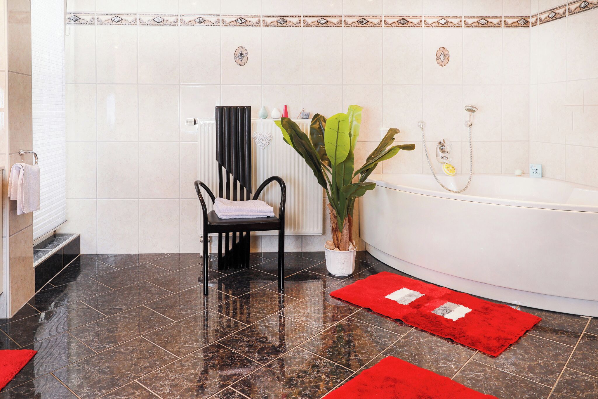 A bathroom with a black chair, a white bathtub, and a red rug.