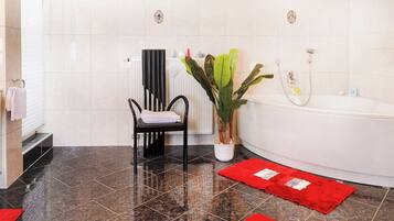 A bathroom with a black chair, a white bathtub, and a red rug.
