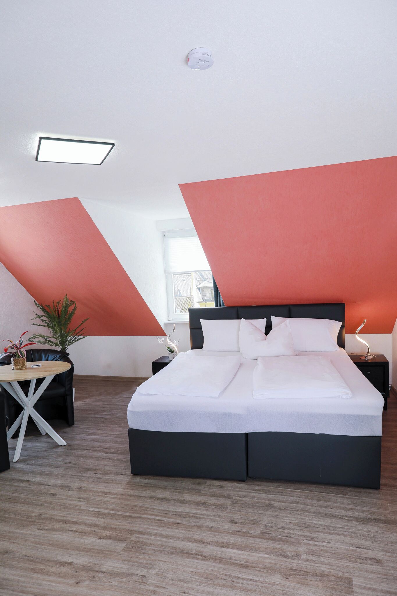 Une chambre moderne avec un grand lit, une petite table et une plante en pot.