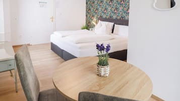 A hotel room with a bed, a round wooden table with a potted plant, and a chair.