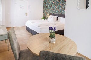 Una habitación de hotel con una cama, una mesa redonda de madera con una planta en maceta y una silla.