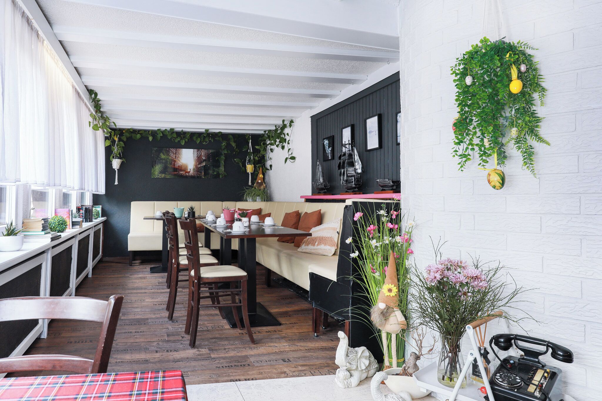 A cozy dining area with a table set for two, a sofa, and a variety of plants and flowers.