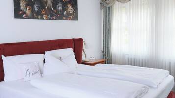 Una cama doble con sábanas blancas, cabecera roja y un cuadro con animales en la pared.