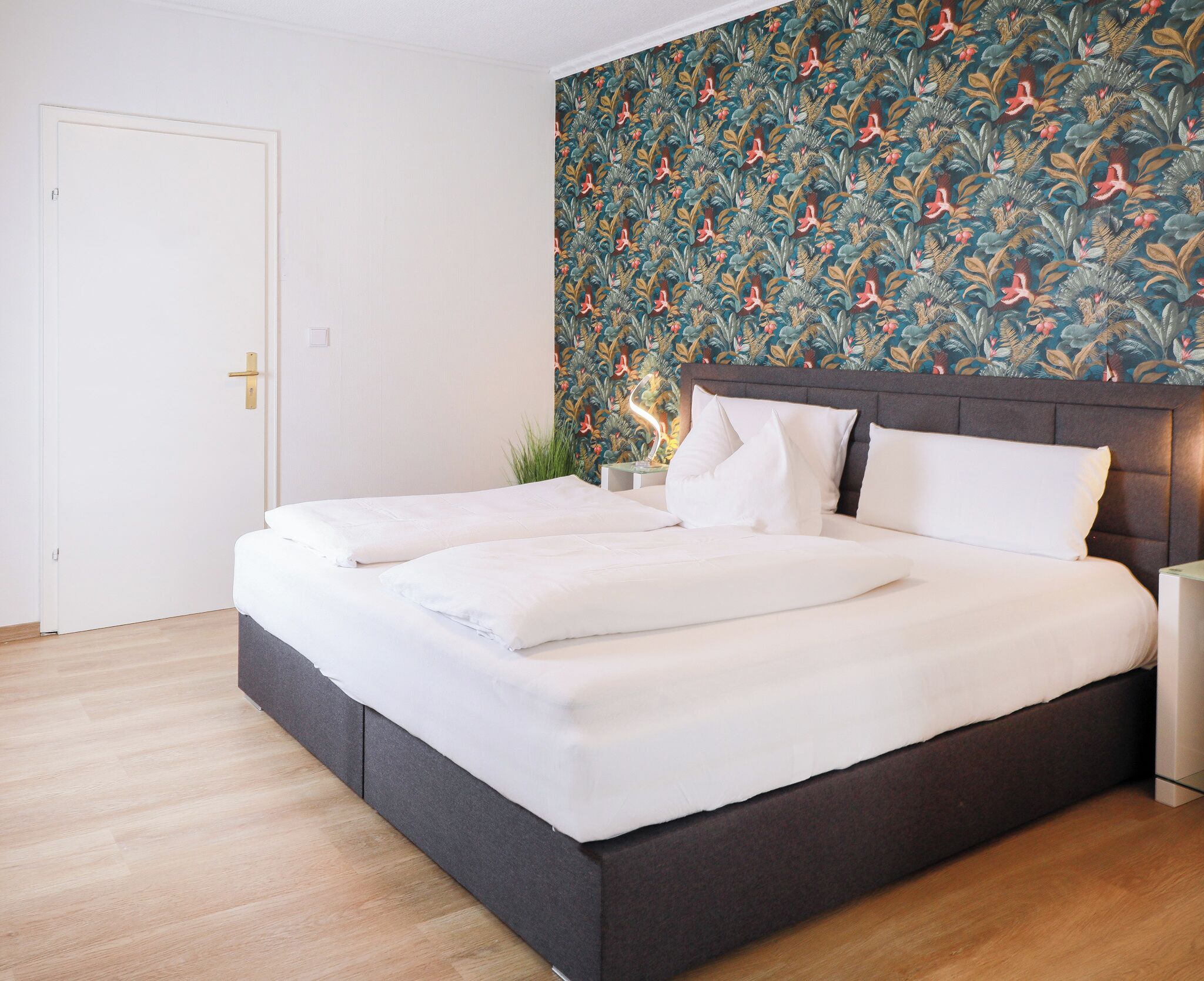 Un dormitorio moderno con una cama grande, un cabecero oscuro y un llamativo papel tapiz tropical.
