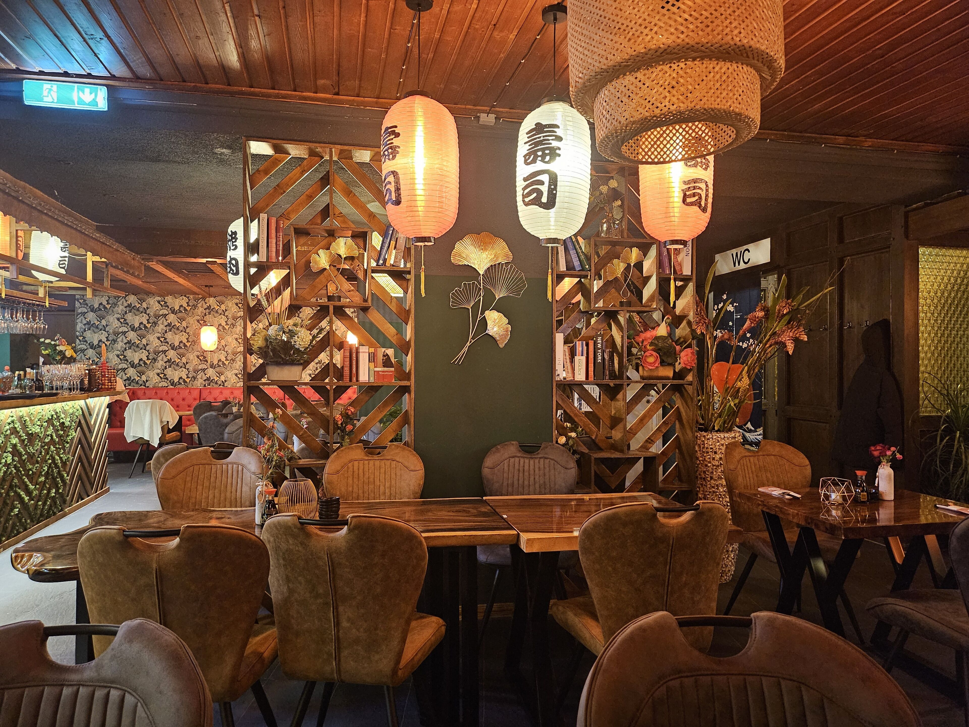 Restaurante com interior em madeira, uma mesa comprida com cadeiras e lanternas penduradas.