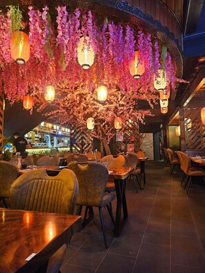 A restaurant with tables and chairs, hanging lanterns, and a bar area in the background. - Schloßschenke (Idar-Oberstein)