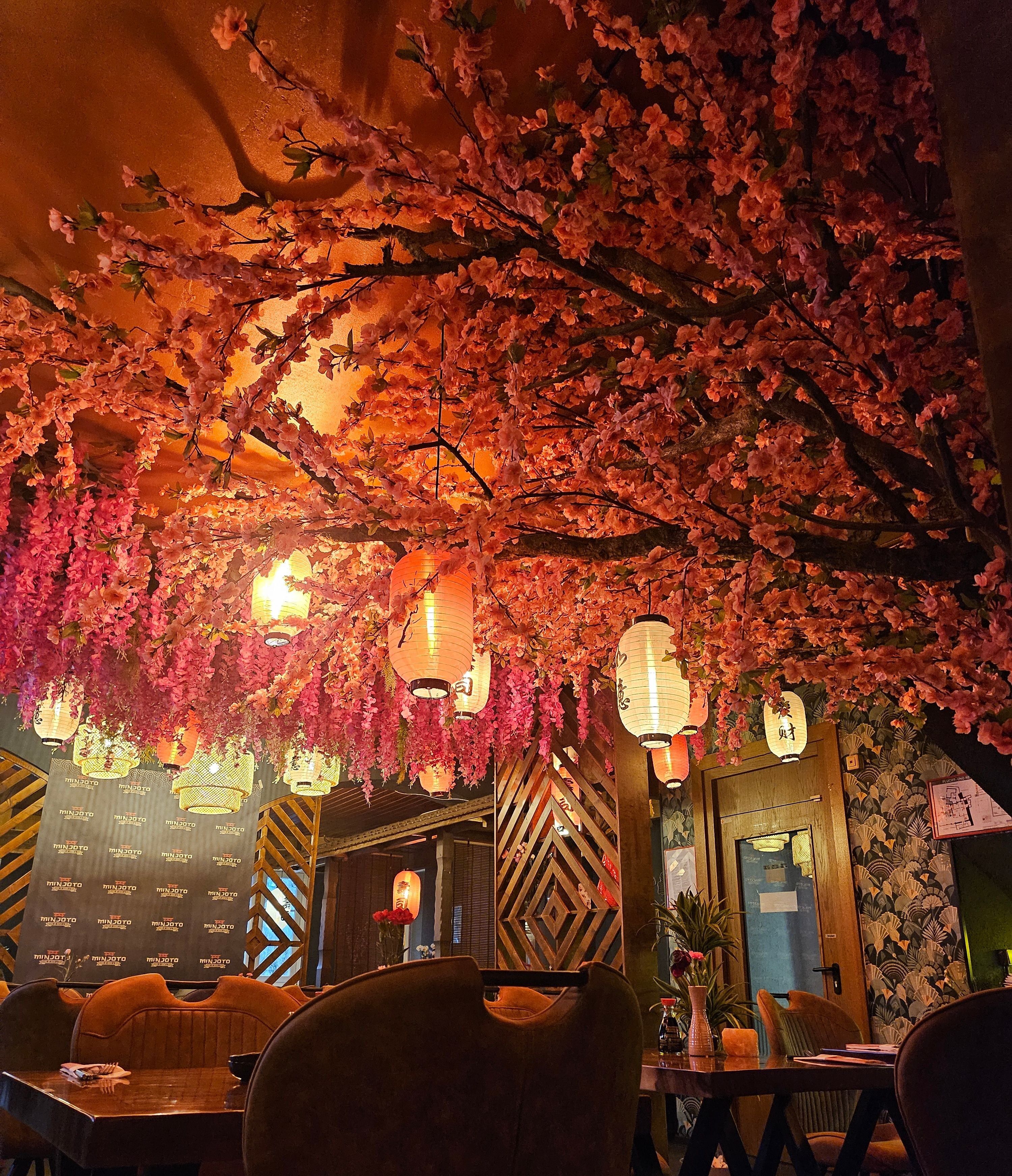 A restaurant with cherry blossom decorations, hanging lanterns, and a wooden interior.